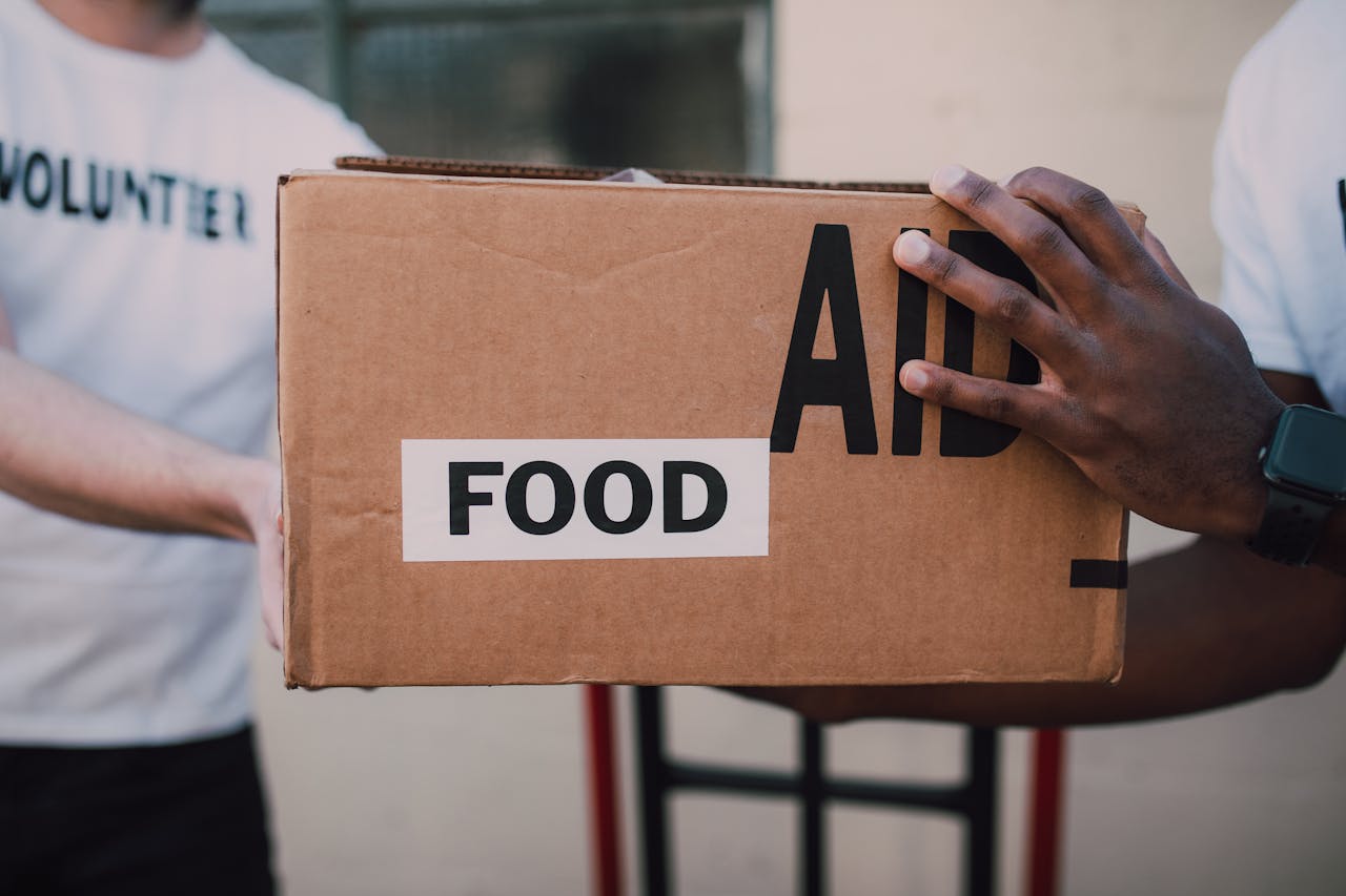 Two volunteers handing over a box labeled 'Food Aid', symbolizing community support.